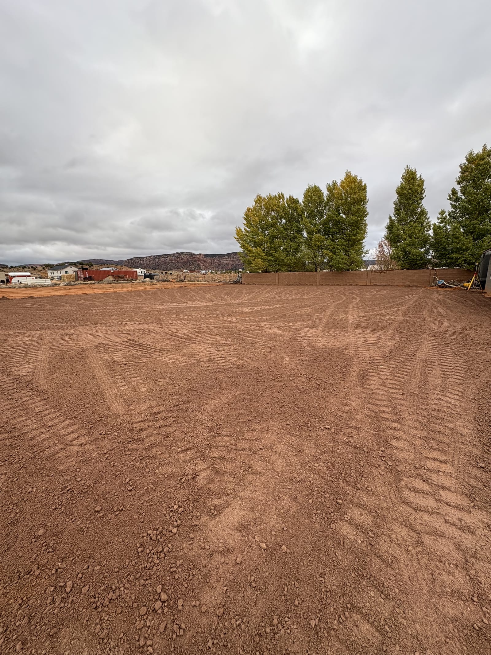 Freshly graded Southern Utah building pad by Roxor South, smooth red dirt with track marks bordered by a perimeter wall and red rock mesas